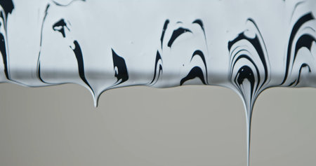 Close up of black and white paint flowing down a pane of glass against a soft grey background,...