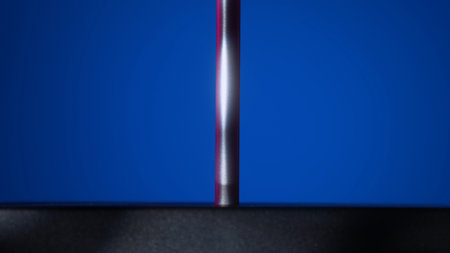 Close up of a minimalist magnetic pendulum stand with metallic rod and black base on a vivid blue...