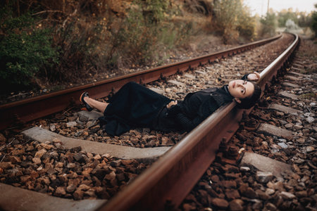 A woman in a vintage dress lies on railroad tracks, creating a dramatic and emotional scene. The...