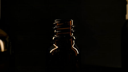 Close up of an empty dark glass medicine bottle with reflective highlights on a black background. Concept of pharmacy, healthcare, addiction, treatment, pharmaceutical industry and medical advertisingの写真素材