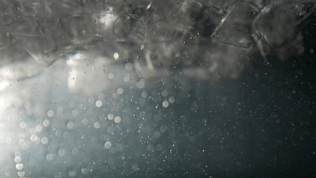 Close up of ice cubes underwater with oxygen bubbles, frost patterns, and soft light reflections....