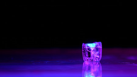 Single ice cube glowing in purple and blue light on a reflective dark surface with copy space....