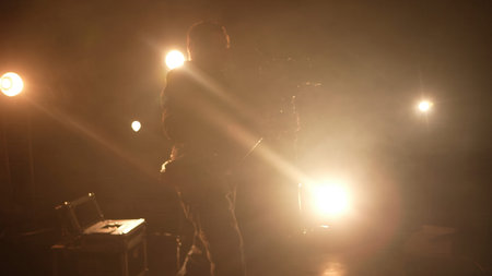 Silhouette of a camera operator filming on a dimly lit stage with spotlights and equipment visible....