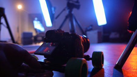 Professional camera mounted on a small dolly with blue and warm stage lights in the background....