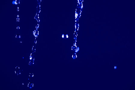 Abstract close up of water drops falling against a dark blue neon background, with glowing...