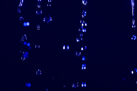 Abstract close up of water drops falling against a dark blue neon background, with glowing...