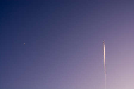 Crescent moon and contrail in the winter evening skyの写真素材
