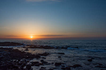 Sunset on the horizon and rocky shore