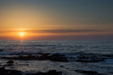 Sunset on the horizon and rocky shoreの写真素材