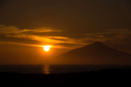 Silhouette of mountains on the sea with the setting sunの写真素材