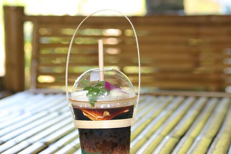 Iced coffee mixed with coconut meat in a clear plastic cup placed on a bamboo table.の写真素材