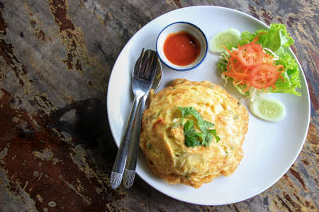 White rice topped with an omelette, aroma of coriander on top, paired with fresh vegetables and chili sauce for added flavor.の写真素材