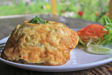White rice topped with an omelette scented with coriander on top, served with fresh vegetables and chili sauce for added flavor.の写真素材