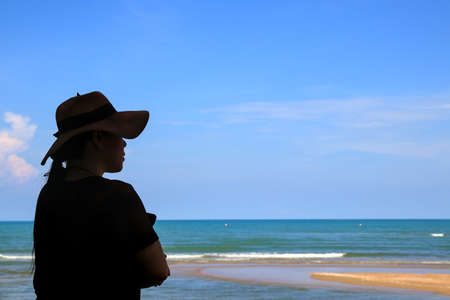 A woman in a wide-brimmed hat stands with her arms folded. Enjoy the nature of the sea and clear sky.の写真素材