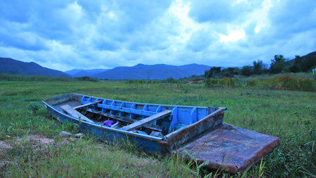An old boat moored in the middle of a meadow. Behind it was a huge mountain and rain clouds began to form.の写真素材