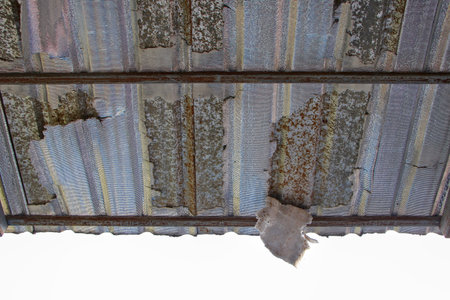 Close-up of a deteriorated corrugated metal roof. Viewed from below, some of the material can be seen hanging down, indicating wear and tear over time.の写真素材