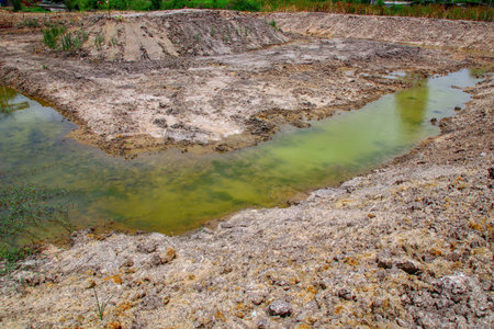 Newly dug wells to store water during the rainy season, some of which still have green water, are surrounded by cracked soil and thin vegetation, under natural light in a rural outdoor area.の写真素材