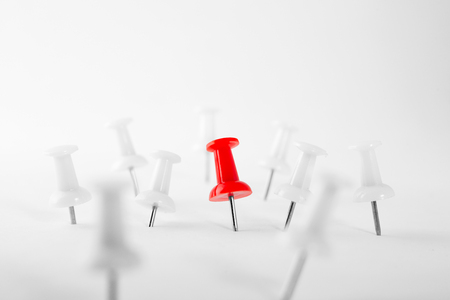 Circle of white Pushpins surrounding red pin, on white background.