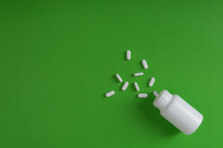 White pills and white bottle with copy space on green background, Healthy and Medicine concept.