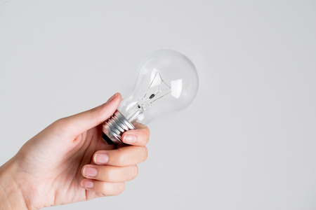 Realistic photo of Light bulb turn on in woman hand giving, isolated on white background.の写真素材