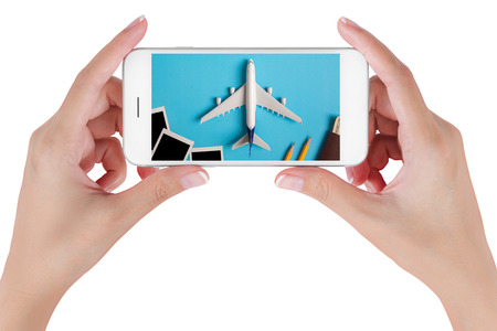 Woman hand using smart phone searching Preparation for Traveling with Blank photograph, airplane, money, passport, pencils and book. Travel concepts, Isolated on white background.の写真素材