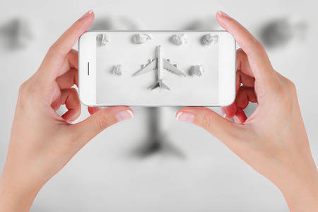 Woman hand using smart phone taking photo for preparation traveling with airplane model flying among paper clouds. Travel concepts, Ambient blurry background.の写真素材