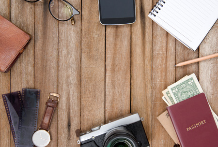 Preparation for travel, mobile phone, money, passport, camera, pencil ,eyeglass, book, Watch, in normal color on wooden table with copy spaceの写真素材