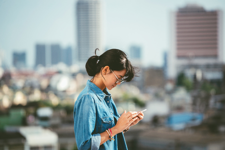 Asian woman used smart phone reads and text message on her smart phone in the city scene background with copy spaceの写真素材