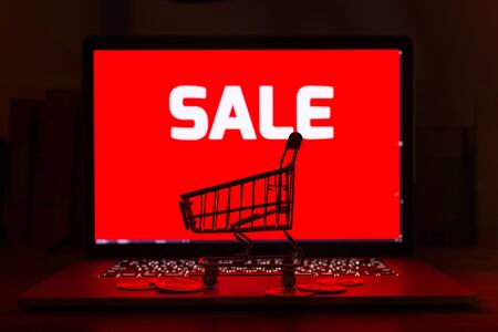 Shopping cart and stack gold bitcoins on computer laptop with a red sale tag on screen background-...