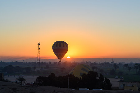 Colorful hot air balloons fly over the green field at sunrise in Valley of the Kings and red cliffs western bank of the Nile river- Luxor- Egyptの写真素材