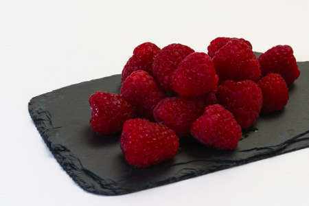 A bunch of red raspberries on a graphite cutting board.