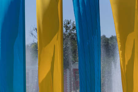 Yellow-blue flags on a background of clear sky and fountain splashes.の写真素材