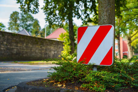 Red and white warning sign in front of an obstacle on the road. Square sign with diagonal stripes.