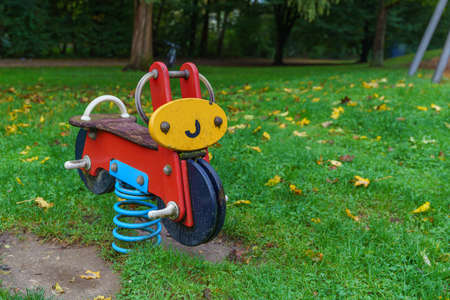 Children's playground in the autumn park. Children's attraction in the form of a bicycle. Yellow foliage on the grass.の写真素材