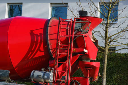 A fragment of a red concrete mixer with a ladder on the car. Against the background of the white...