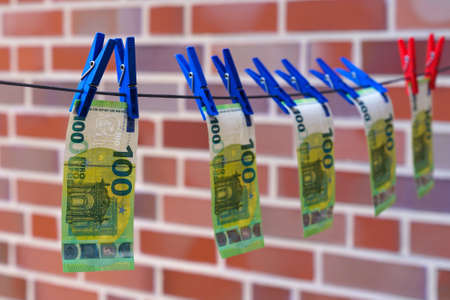 One hundred euro bills are dried on a string against a brick wall. Blue clothespins.の写真素材