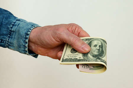A man's hand holds out a bundle of one hundred dollar bills. Close up.