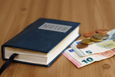 Notebook on the table next to euro banknotes and coins. Close up.