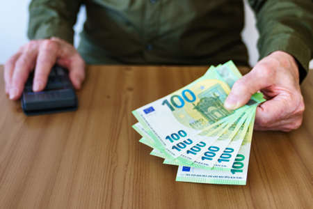 Man's hand with the bills of one hundred euros. Calculator in the right hand.