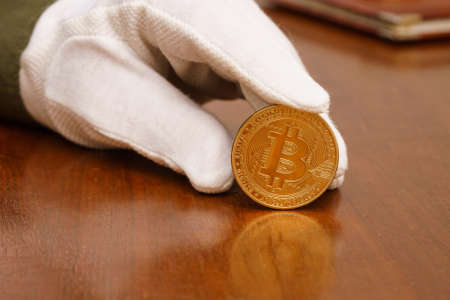 A hand in a white glove holds a bitcoin. Close up.