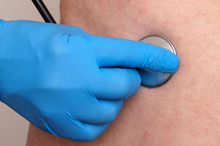 A doctor's hand in a blue glove holds a stethoscope on the patient's body. Closeup.