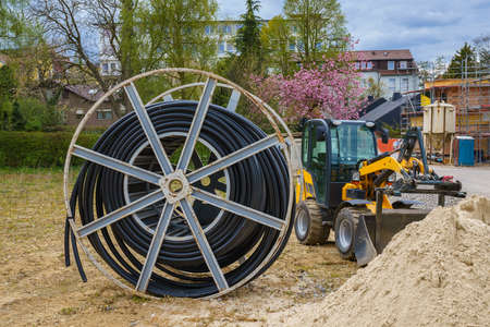 Cable for electric power supply on wooden spool on a construction site. Small yellow excavator a...