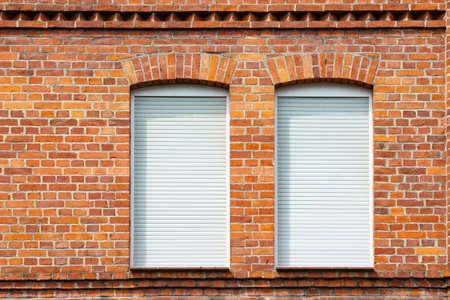 Fragment of a brick wall of a building with two windows. The windows are covered with white blinds.の写真素材