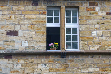 View of a stone wall with a window. A pot of flowers outside on the windowsill.