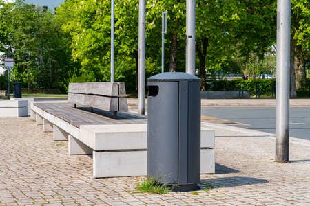 A metal trash bin and a long bench in an empty city park.の写真素材