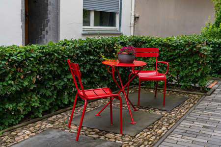Two metal chairs and a table painted with red paint in the courtyard of the house. Surrounded by green vegetation.の写真素材