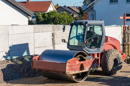 The compact road roller standing on a construction site near a concrete fence.