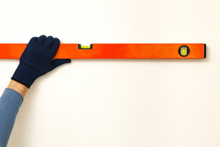 Male glove hand holding building level near white wall. Close up.の写真素材
