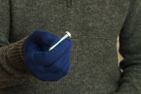 Human hand in blue protective gloves holding a large metal bolt. Close up.の写真素材