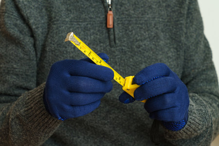 Yellow tape measure in male hands in blue gloves. Close up.